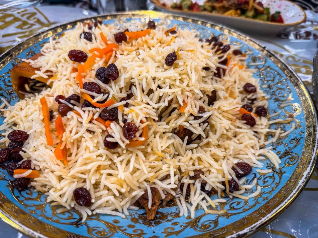 Afghan mutton pulao with separate grains of basmati, dark raisins and julienned carrot on a blue and gold platter