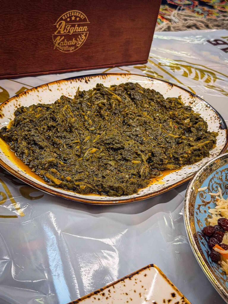 Plate of Afghani palak, dark braised greens sitting in pools of mustard yellow oil, at Afghan Kabab Village Dubai