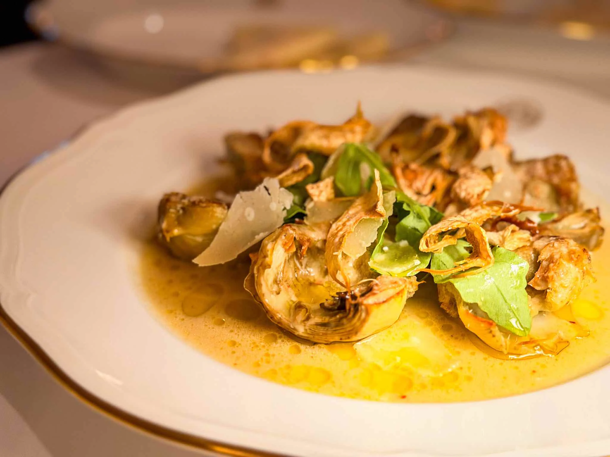 Plate of artichoke hearts in a light sauce with rocket leaves and shaved Parmesan.