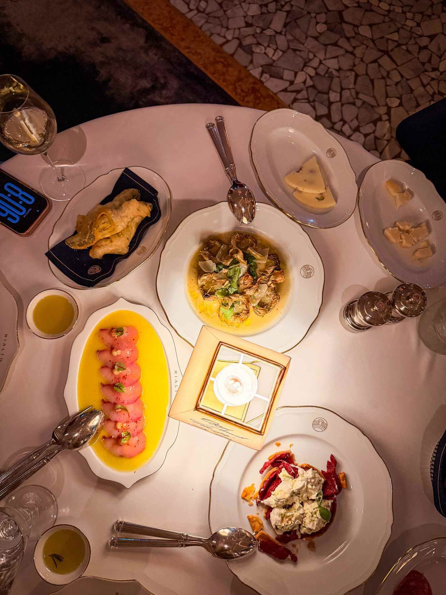 Overhead view of several Rialto starter dishes on a white tablecloth, including yellowtail crudo, artichokes, fried courgette flowers and tomato tart.