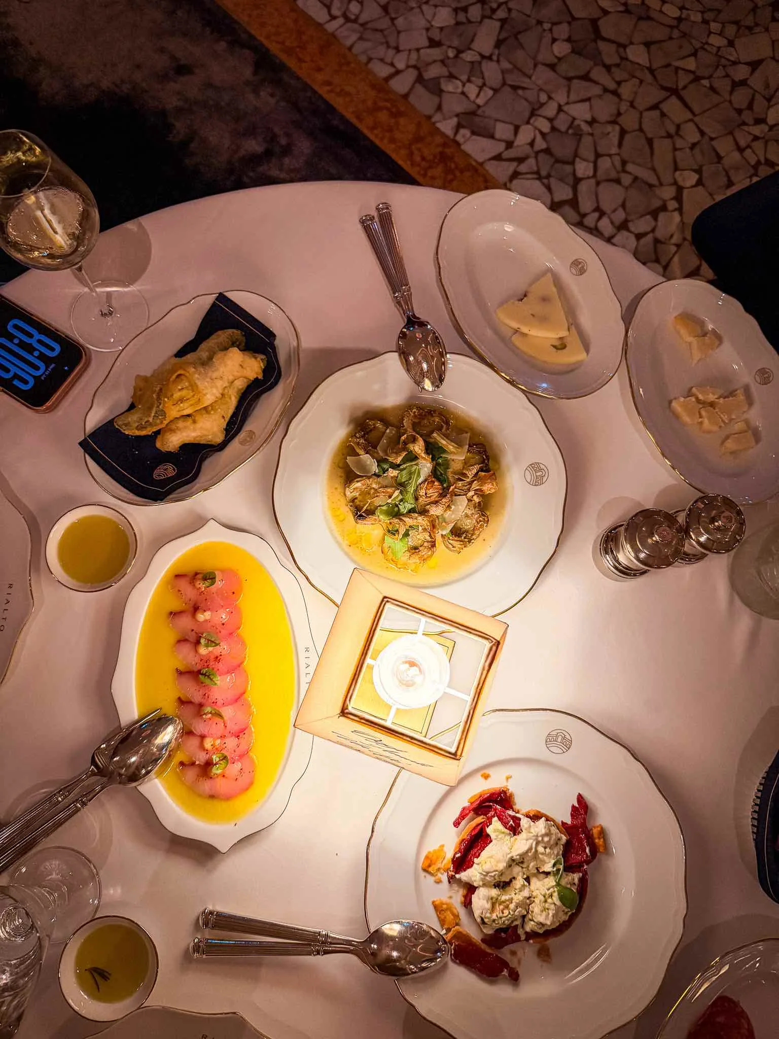 Overhead view of several Rialto starter dishes on a white tablecloth, including yellowtail crudo, artichokes, fried courgette flowers and tomato tart.