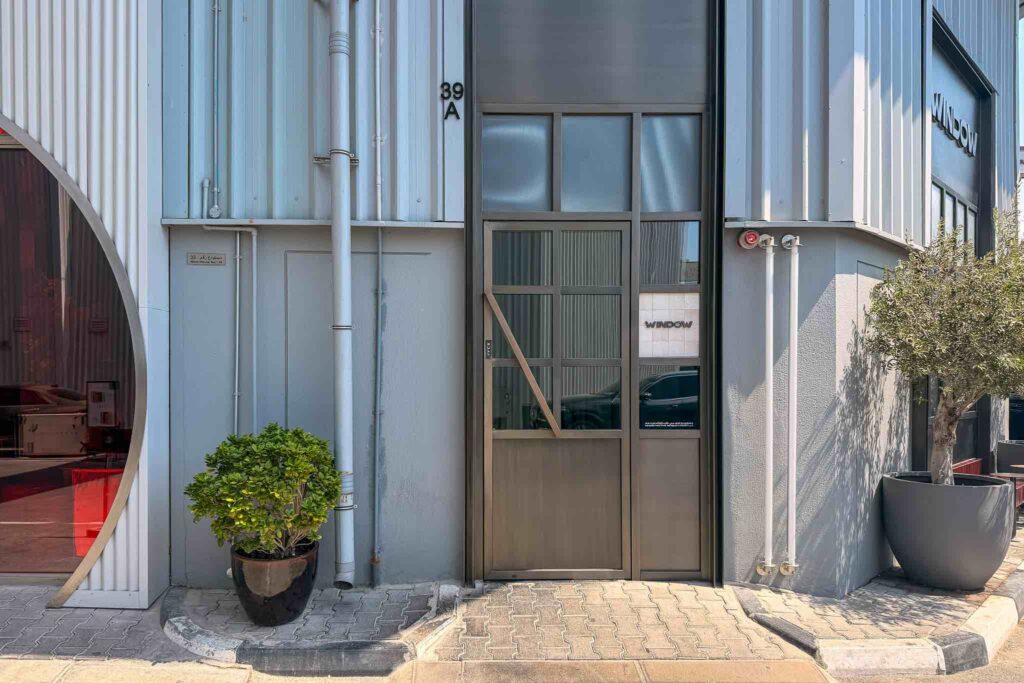 Entrance to Window restaurant at Warehouse 39A, Alserkal Avenue, Al Quoz, Dubai, with a grey corrugated metal facade and a potted olive tree