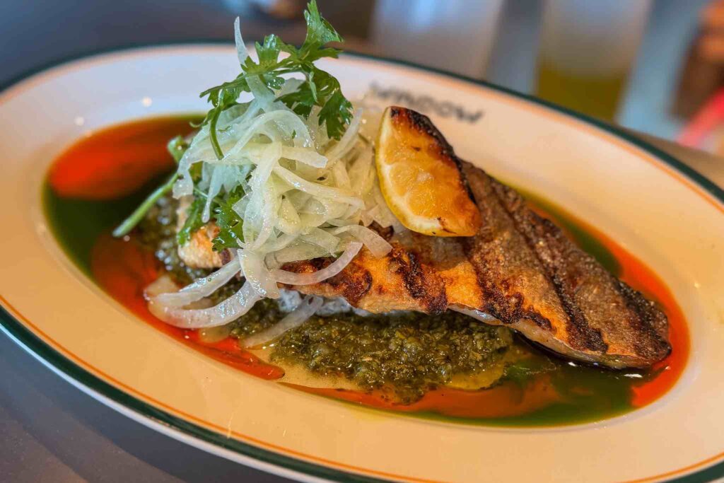 Grill-marked sea bass fillet with shaved fennel, coriander and charred lemon over a green herb sauce and red oil