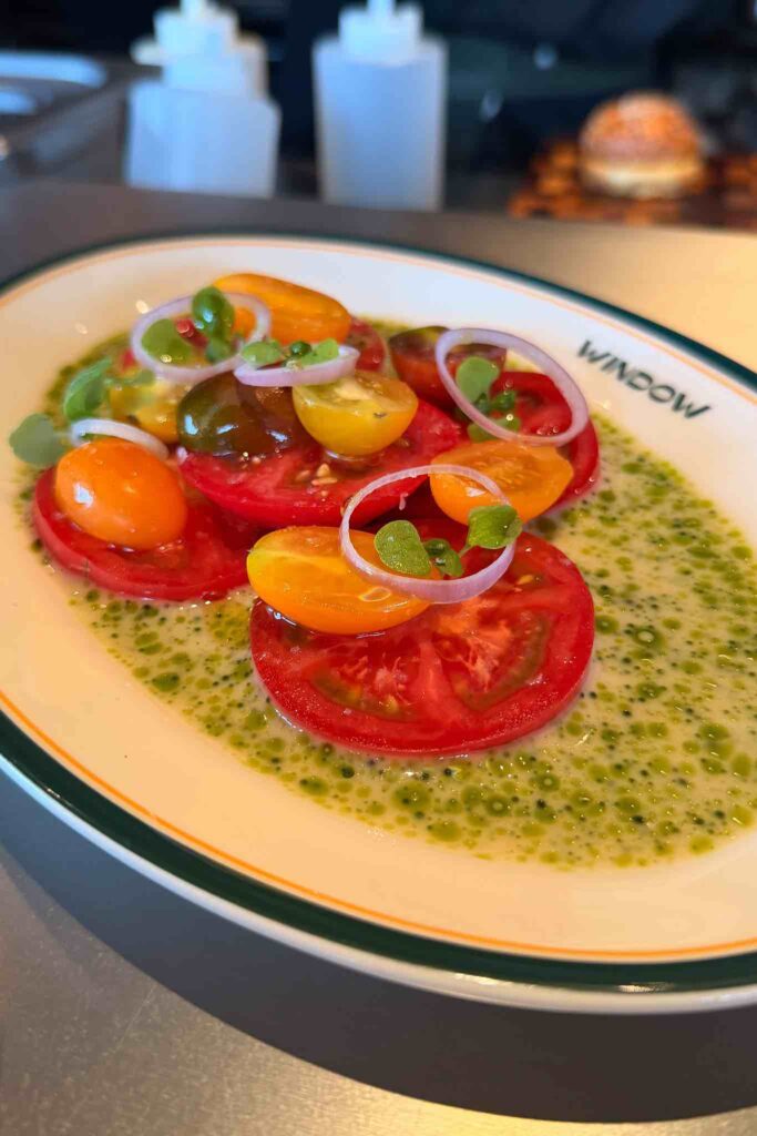 Sliced red and yellow heirloom tomatoes with shallot rings and small basil leaves in a green herb oil dressing