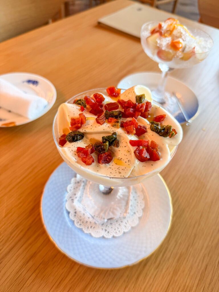 Olive oil ice cream with hoshigaki and candied olives in a glass coupe, with a coupe of iced fruit behind, at Blue restaurant, Saadiyat
