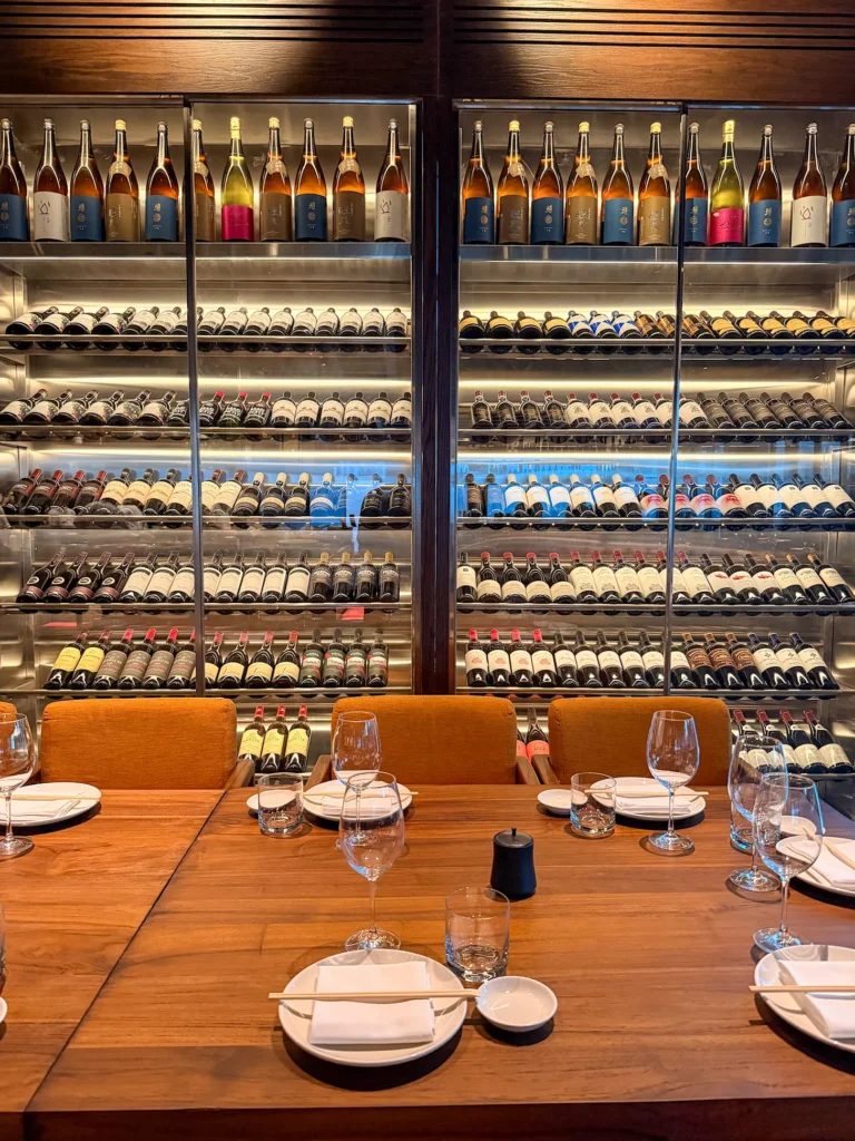 Floor-to-ceiling glass wall of sake and wine bottles behind a set dining table at Noren, Japanese restaurant at the Pullman JLT, Dubai