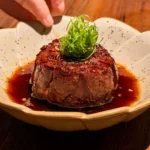 Robata-grilled Australian beef tenderloin in a pool of glossy Japanese barbecue sauce, topped with fine spring onion and chilli flakes, in a speckled bowl at Noren in JLT