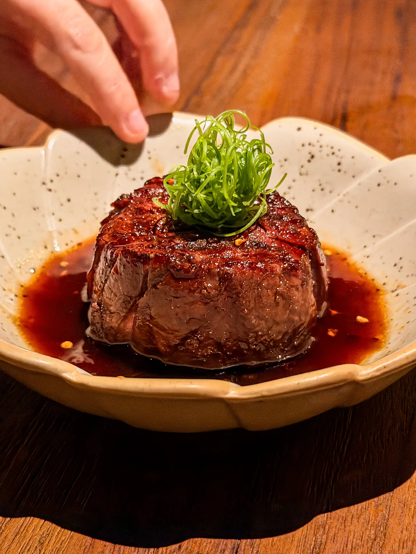 Robata-grilled Australian beef tenderloin in a pool of glossy Japanese barbecue sauce, topped with fine spring onion and chilli flakes, in a speckled bowl at Noren in JLT