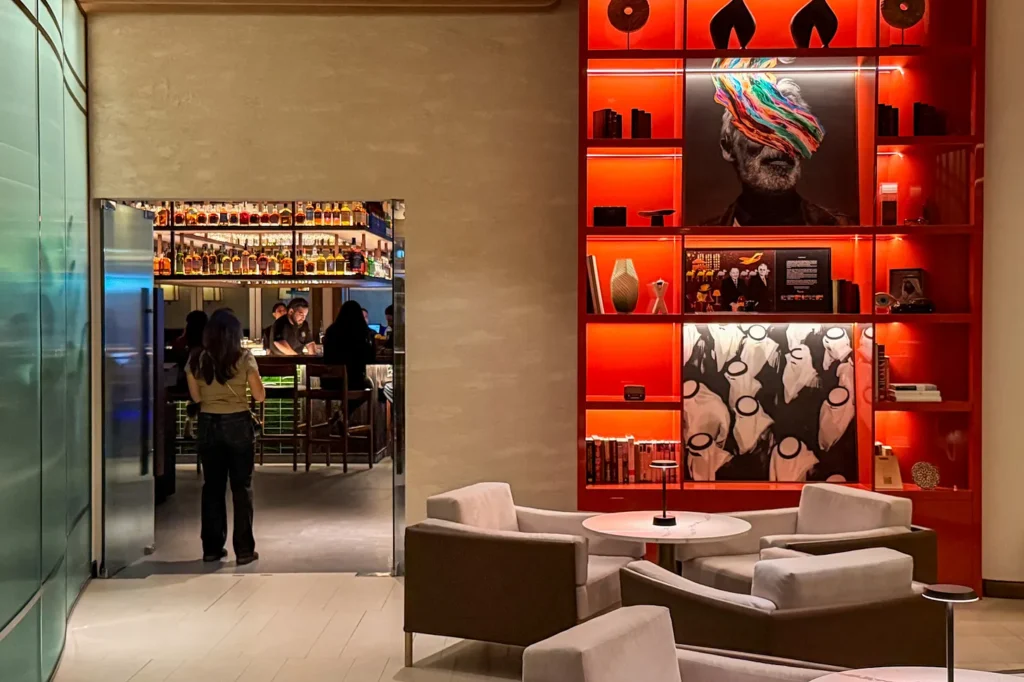 The entrance to Noren from the Pullman Dubai Jumeirah Lakes Towers lobby, opening onto the bar, beside a red-lit shelf of artwork and lounge armchairs