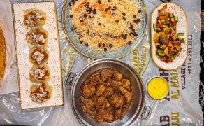 Overhead view of an Afghan meal for two on a plastic-covered carpet: pulao, charsi karahi, mantu, palak, naan, salad and fruit