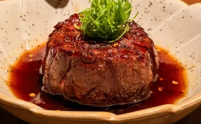 Robata-grilled Australian beef tenderloin in a pool of glossy Japanese barbecue sauce, topped with fine spring onion and chilli flakes, in a speckled bowl at Noren in JLT